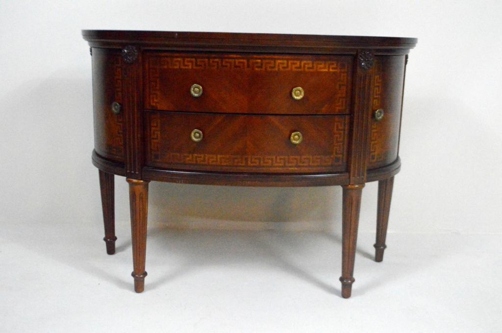 George III Style Mahogany Demilune Sideboard: The banded demilune top with a half star inlay over a shaped apron with two drawers and two bottle doors each banded with a Hellenic key inlay, the whole raised on four turned and reeded tapering legs