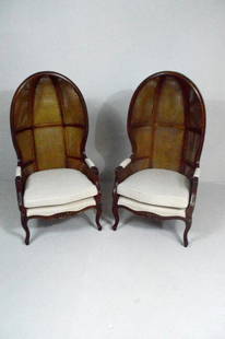 Pair of Rattan Porter Chairs: Each with double sided rattan balloon enclosure backs, over a single cushion, the whole raised on four cabriole legs ending in peg feet.