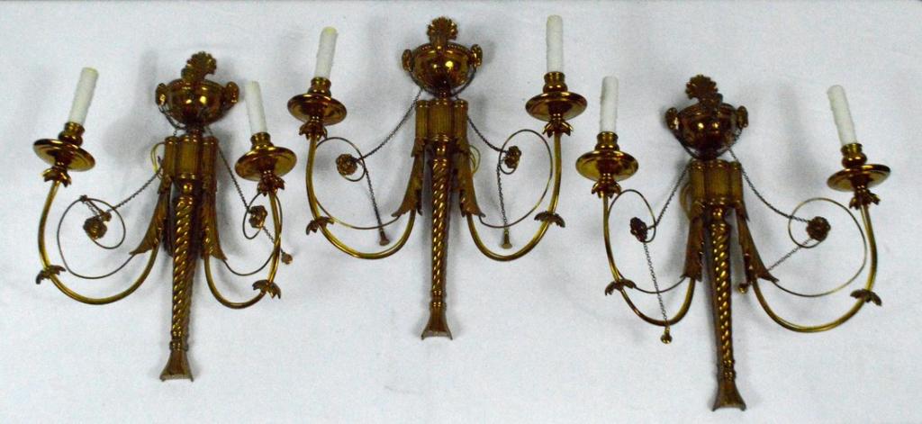 Three Brass Two Light Sconces: Wired. Each with an urn final over reeded column with two scrolling arms ending in wax pans and brass capitals.