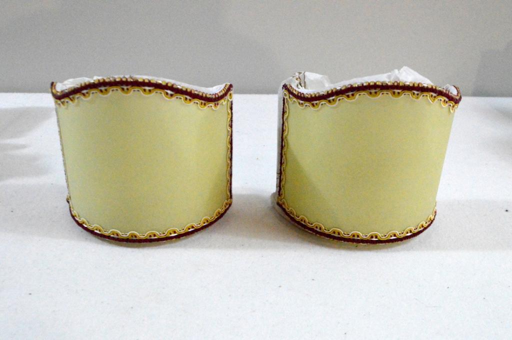Four Fortuny Sconce Shades: Of usual form, ecru with gold and maroon piping to edges, in original Fortuny paper, never used.