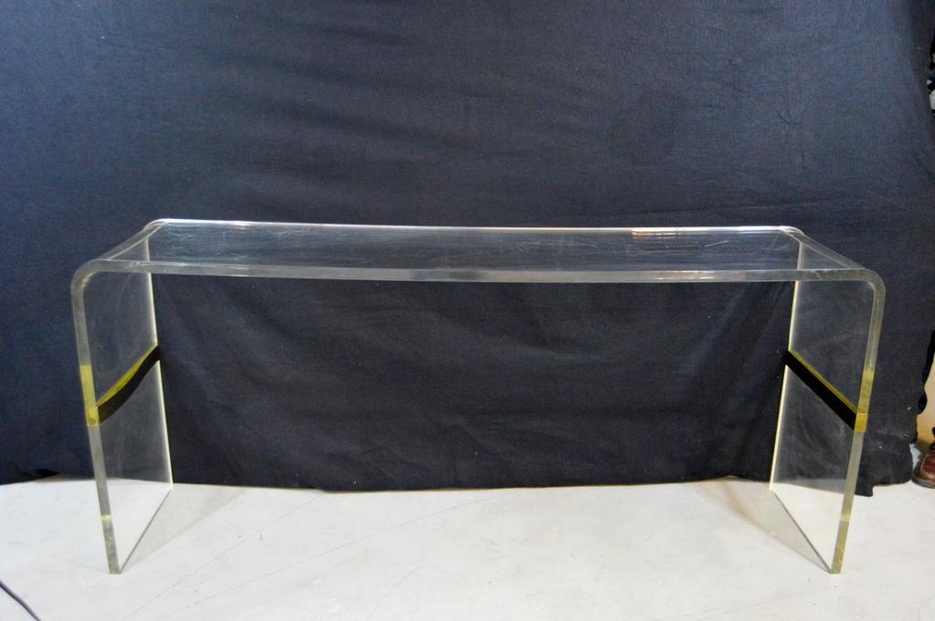 Lucite Sofa Table: Of a single piece, with rounded and moulded edges, with a brass moulding half way down legs.