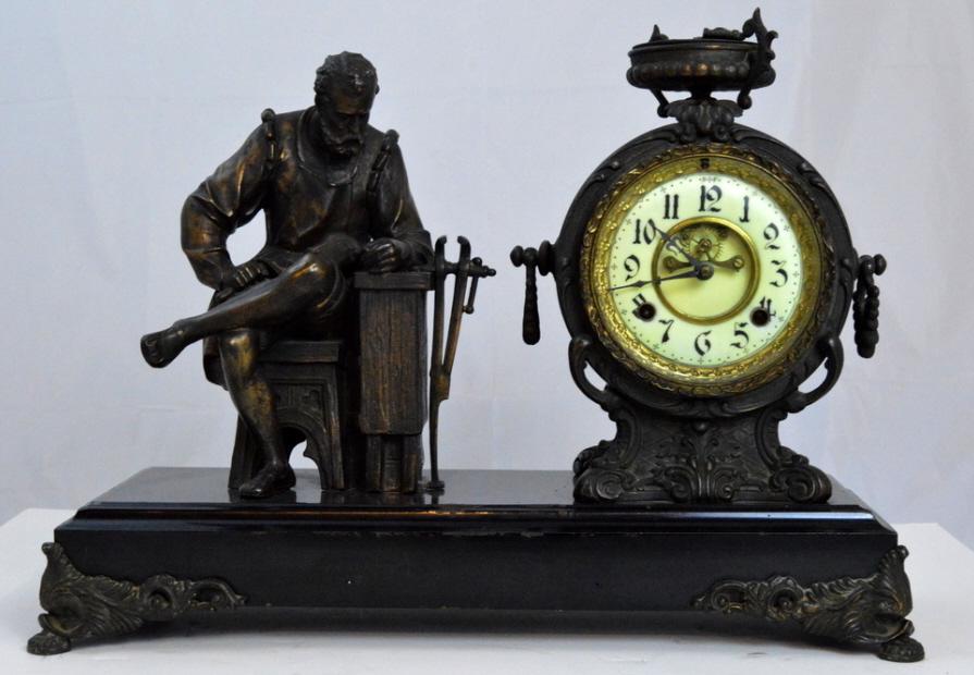 Figurative Mantle Clock: With an enameled face with Arabic numerals, of a metal smith pondering over a ewer while sitting at his bench, the clock surmounted by an urn, raised on a black metal base raised on ornate bracket fee