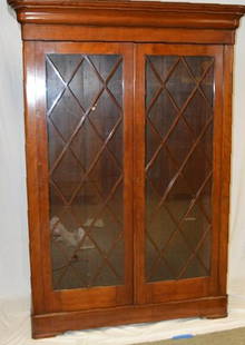 Late Federal Glazed Cherry Bookcase: With a moulded cornice over a pair of lattice work glazed doors opening to reveal five shelves, on a rounded rectangular base raised on bracket feet. 87 x 56 x 18.5 in. Property of the Junior