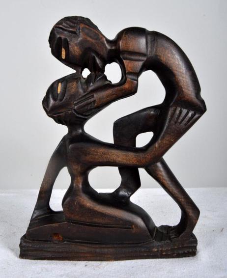 African Statue of Man and Woman Intertwined: Modern; The wooden statue of a man leaning over and kissing a woman who has her arm embraced around him, carved into the base. The eyes are carved slightly in 10 x 7 x 1.5 in. Condition: Wear consiste
