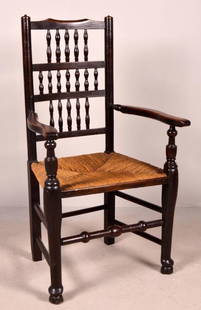 English Provincial Caned Oak Arm Chair: Early 19th Century, with a shaped crest rail over three layers of spindles, the shaped arms with turned stumps flanking the caned seat, the whole raised on round legs supported by turned stretchers.