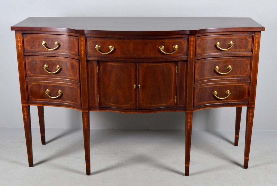 Federal Style Inlaid Mahogany Sideboard: The shaped top is over a single drawer and pair of doors, flanked on each side by a dingle drawer over a bottle drawer. The whole raised on six tapering legs inlaid with bellflowers. Oak secondary woo