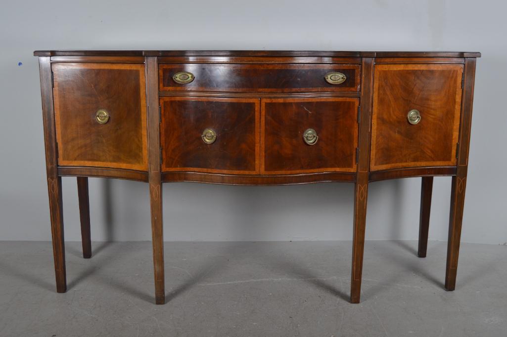 George III Style Mahogany Sideboard: Serpentine reeded edge top, with a single center drawer over cabinet, flanked by tall cabinets. Brass oval bail pulls, with burl veneer border to cabinet doors. Raised on six tapered legs with string 