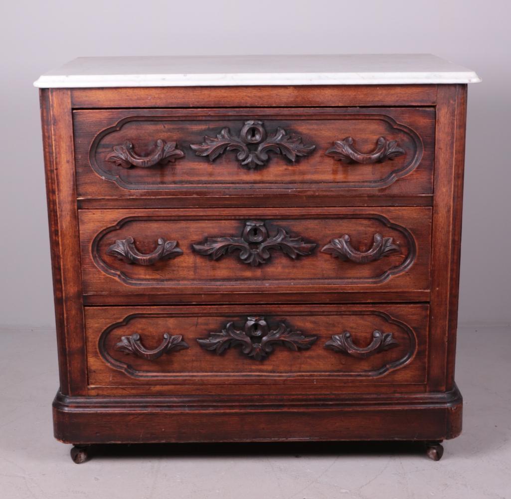 Renaissance Revival Chest of Drawers: With a marble top over three carved drawers, the whole raised on a plinth with casters Dimensions: 31 x 32.5 x 18 in. NOTE: Wear consistent with age and use
