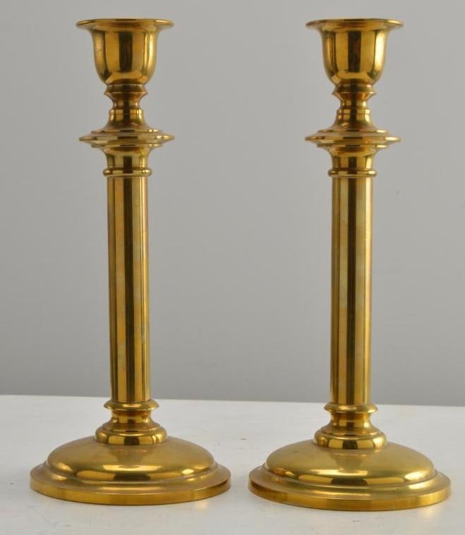 Pair of Brass Candlesticks: Each with a plain capital over a single plain column, raised on a round base. Dimensions: H 11.5 x W 5.5 x D 5.5 inches NOTE: Wear consistent with age and use.