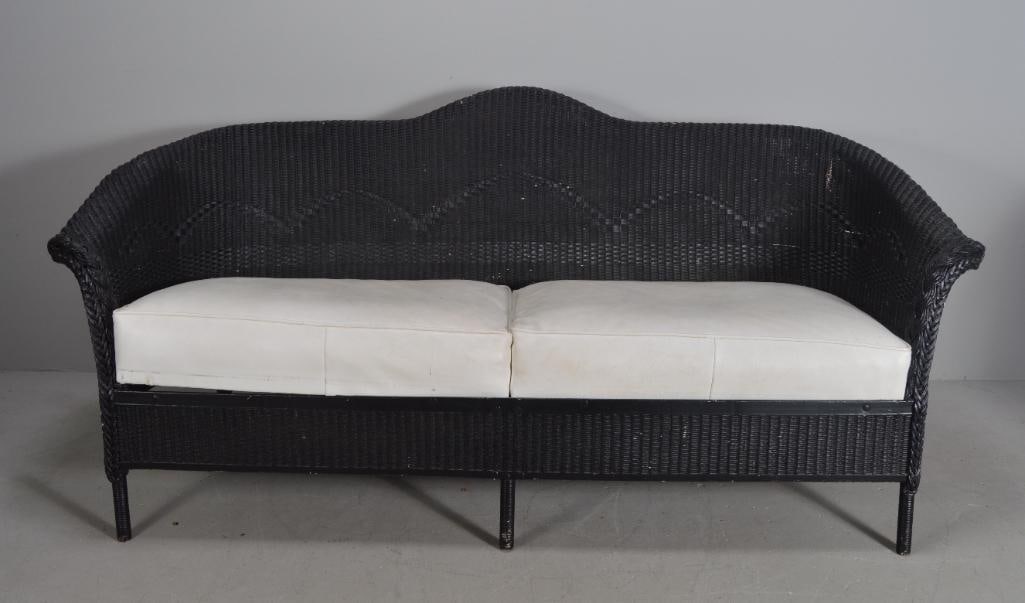 Black Wicker Sofa: With a shaped crestrail over shaped arms and plain apron, with white slip in cushions, raised on four turned legsDimensions: H 33 x W 62 x D 29 inchesNOTE: Paint missing in places, some losses to wick