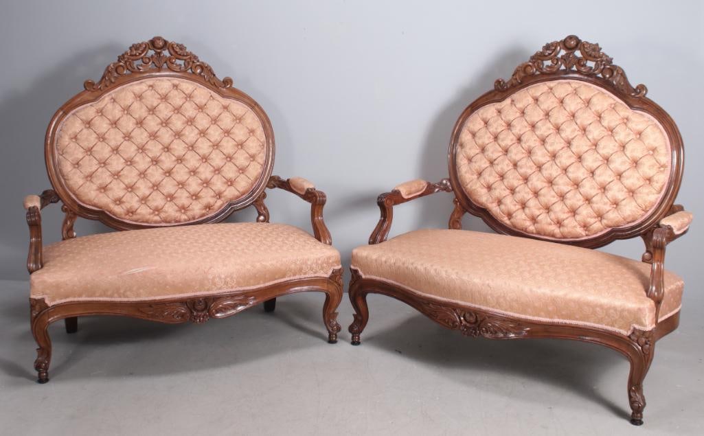 Pair of Renaissance Revival Settees: Each with a carved and shaped crestrail over a tufted back, the upholstered seat flanked by carved arms and over a carved and shaped apron, the whole raised on four carved cabriole legs ending in peg