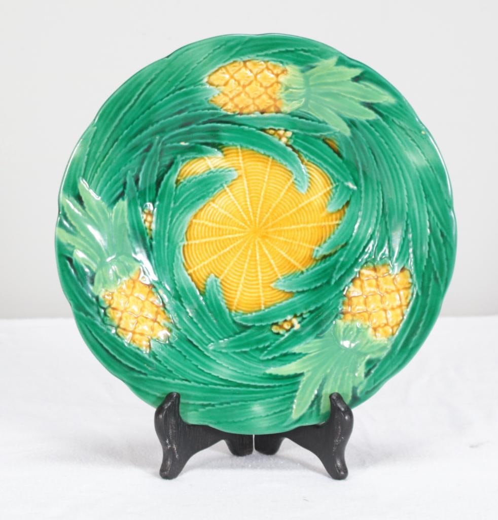 George Jones Pineapple Majolica Plate: Featuring a border of green leaves revealing three pineapples with yellow basket weave center. Mark on back. Dimensions: H 9 x W 9 x D 2 inchesNOTE: Good. See photos