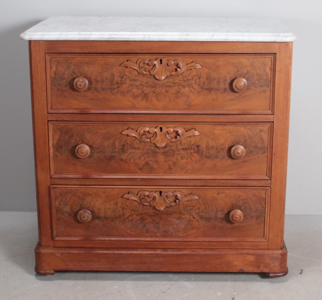 Eastlake Walnut Chest of Drawers: With a moulded marble top over three reeded drawers with carved escutcheons, raised on a rounded plinth. Dimensions: H 31 x W 32 x D 18 inches NOTE: