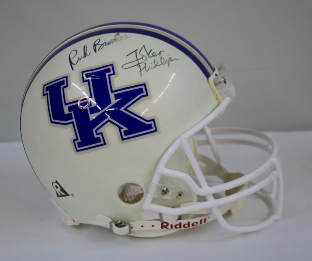 Rich Brooks and Joker Phillips Dual-Signed UK Helmet: Vintage white Riddell Kentucky Wildcats full-size football helmet with blue and gold center striping and large “UK” decals, signed in black marker by former Kentucky head coaches Rich Brooks a