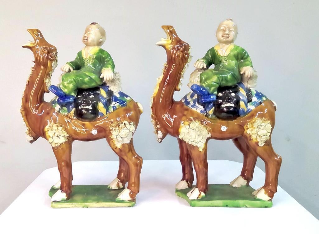 Pair of Chinese Glazed Figures of Boys Riding Camels: Pair of polychrome glazed ceramic figures depicting boys in green robes seated atop camels. The camels modeled with raised head and textured applied decoration along the body, standing on integral