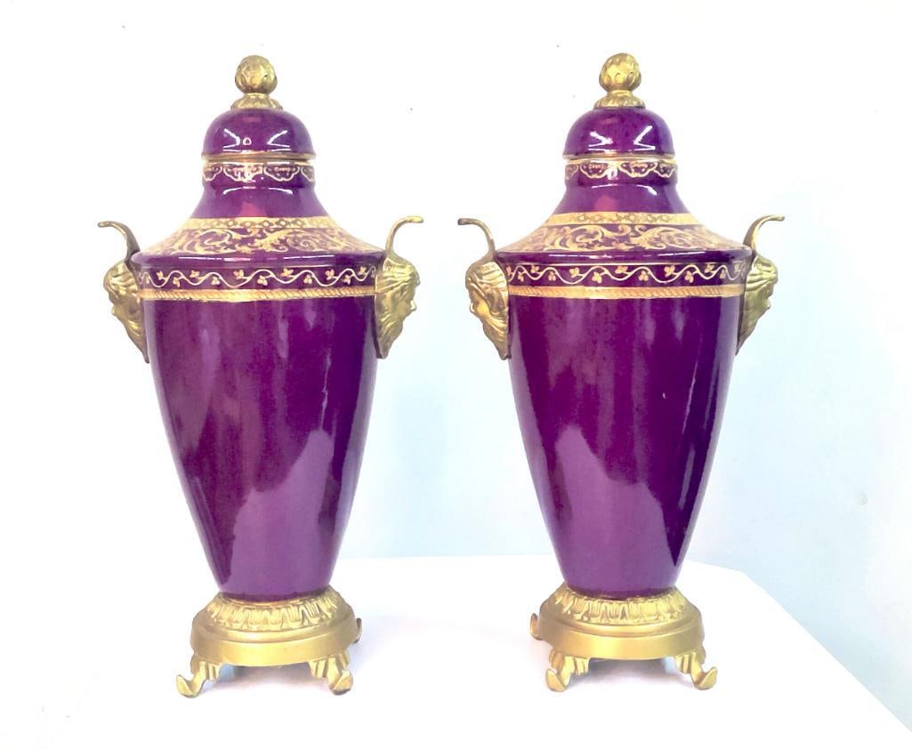 Pair of Dresden Porcelain Urn-Form Vases with Gilt Mounts: Decorative pair of covered porcelain urns with deep purple glaze and extensive gilt decoration in scrolling foliate patterns. Each fitted with gilt metal mounts including mask-form handles and raised