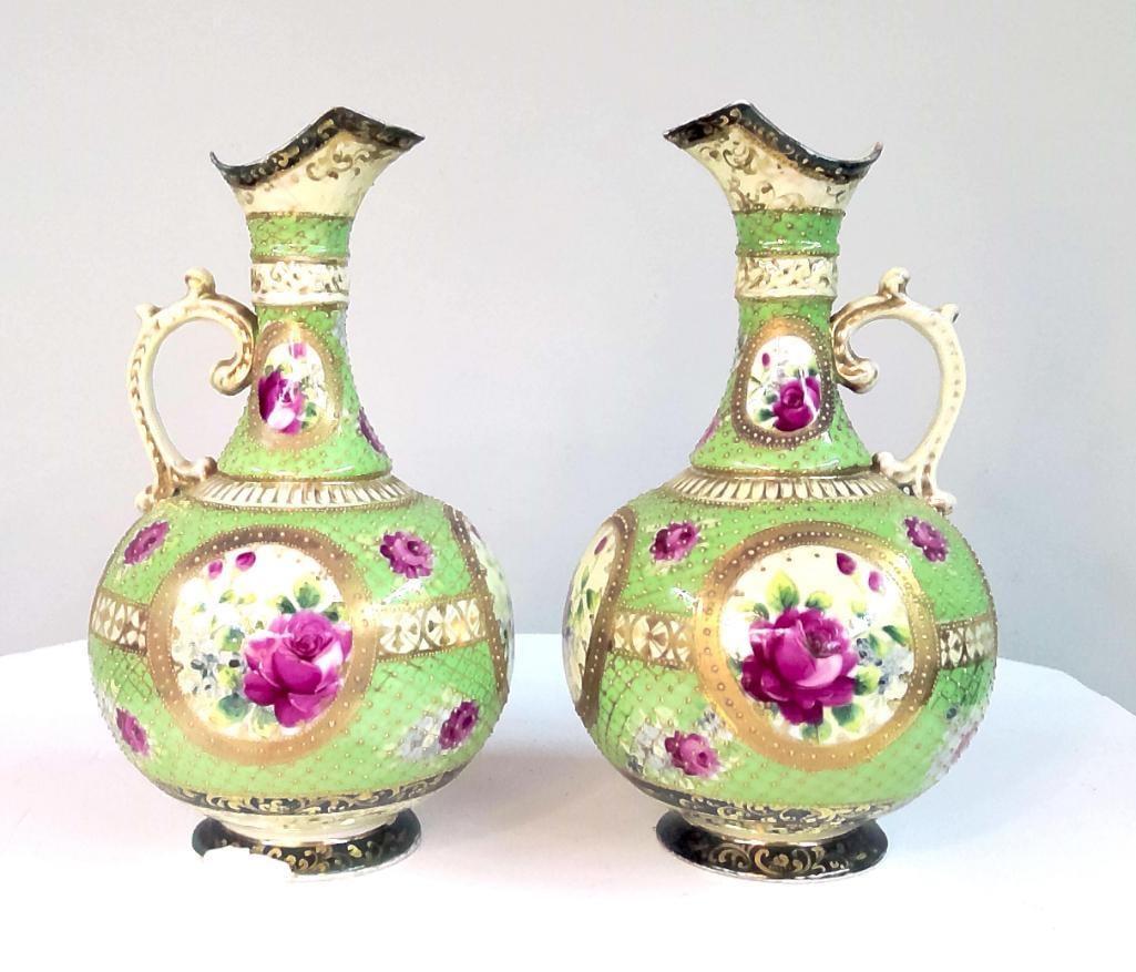 Pair of Victorian Style Hand-Painted Porcelain Floral Ewers: Pair of porcelain ewers with bulbous bodies, tall flared necks, and molded handles. The bodies decorated with hand-painted rose medallions within gilt borders on a green ground with gilt lattice and