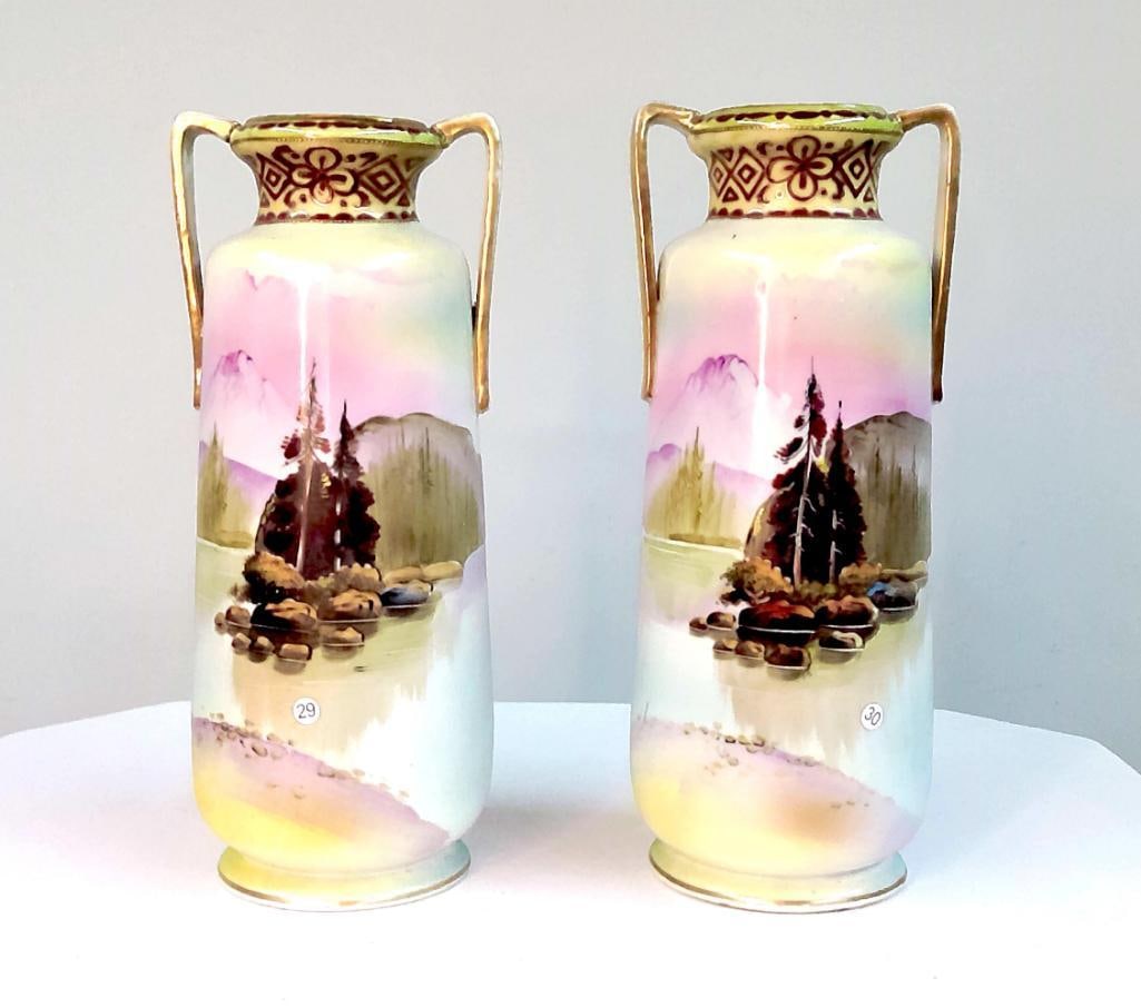 Pair of Hand-Painted Porcelain Landscape Vases: Pair of porcelain vases of cylindrical form with flared rims and applied double handles. Each decorated with hand-painted landscape scenes depicting lakeside settings with trees and distant mountains 