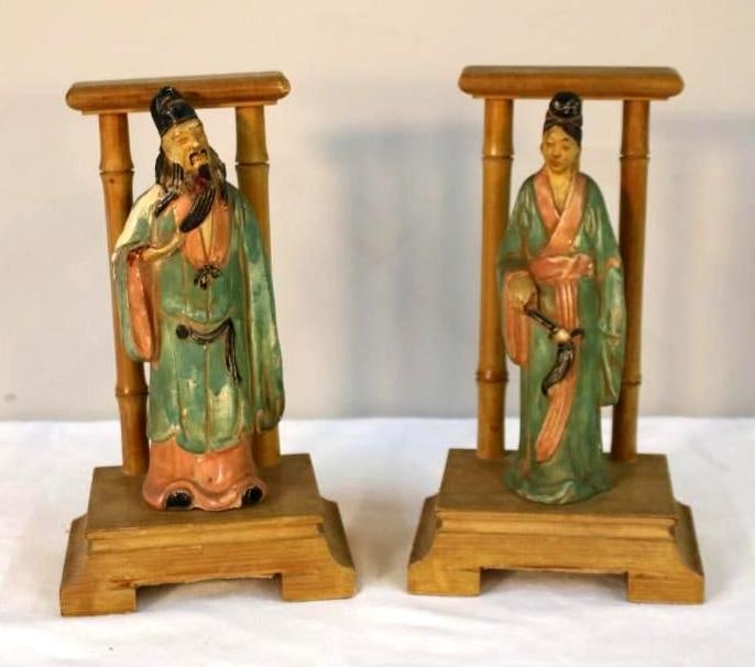 Pair of Chinese-Style Painted Ceramic Figures: A matched pair of polychrome-painted ceramic figures depicting a male scholar and a female attendant, each standing within a simple architectural-style frame mounted on a stepped wooden base. The