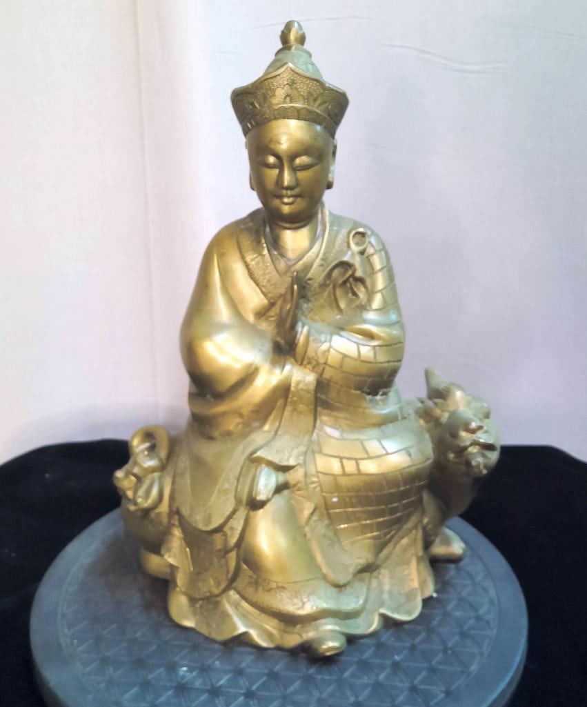 Buddha Seated on a Foo Dog (Guardian Lion): Castfigure depicting a seated Buddha in a contemplative pose, hands together, mounted on a stylized foo dog (guardian lion). The figure wears a headdress and flowing robes with incised decorative deta