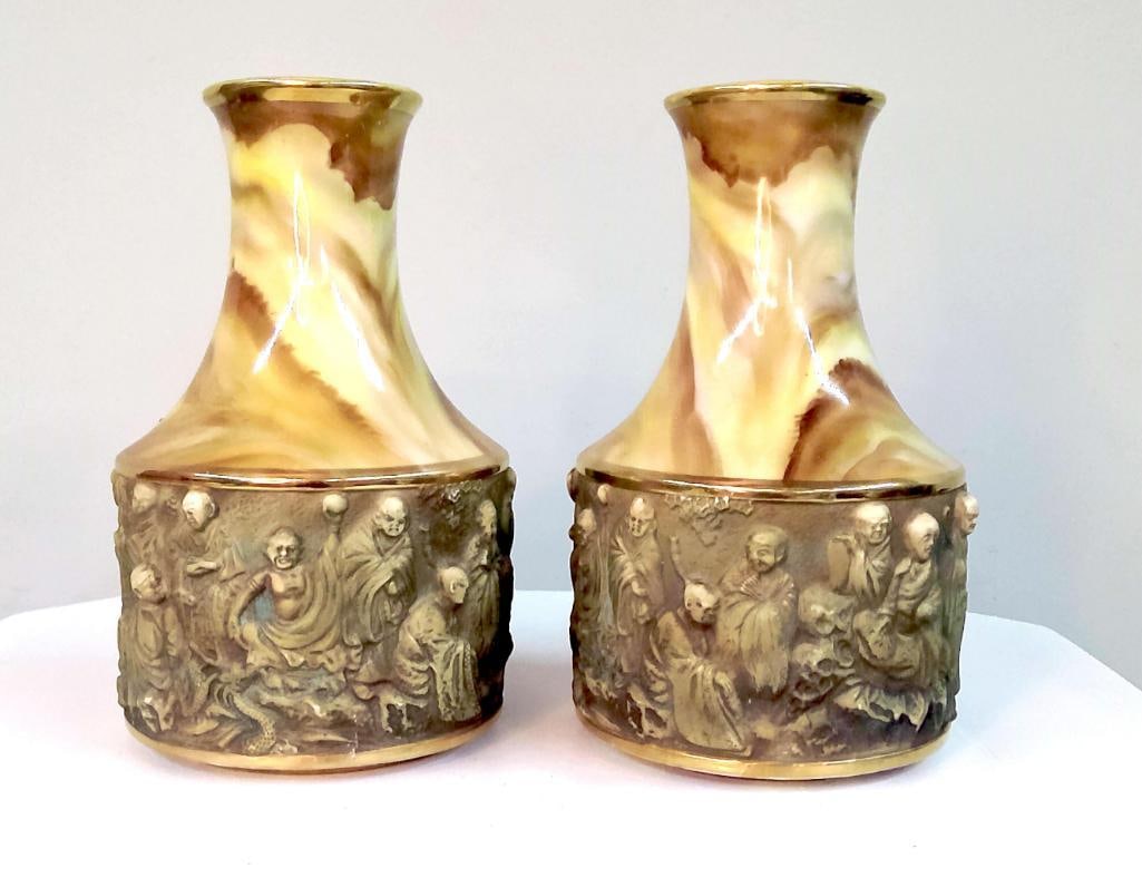 Pair of Porcelain Vases with Arhat Relief Decoration: Pair of porcelain vases with flared necks and marbled brown and cream glaze to the upper bodies. The lower sections decorated with continuous molded relief scenes depicting Buddhist arhats (Luohan) in