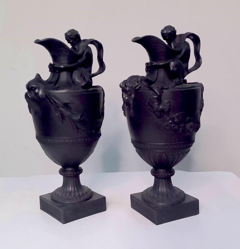 Pair of Wedgwood Black Basalt Figural Vases, Nos. 107 and 109: Pair of Wedgwood black basalt pedestal vases comprising complementary models No. 107 and No. 109. Each vase features a seated female figure supporting a cornucopia-form handle above an ovoid body deco