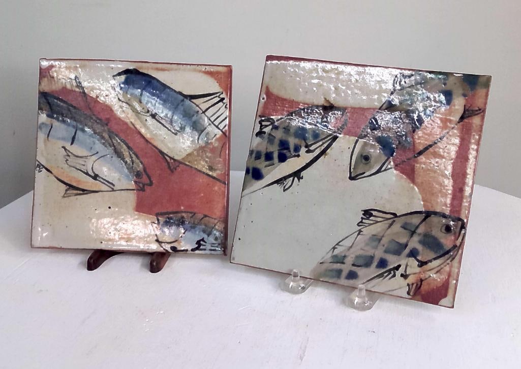 Pair of Studio Pottery Fish Decorated Ceramic Tiles: Two hand-painted ceramic art tiles depicting fish in an aquatic composition, executed in blue, black, cream, and iron-red glazes. Dimensions: H 7 x W 7.5 x D inches NOTE: Minor expected wear. No signi