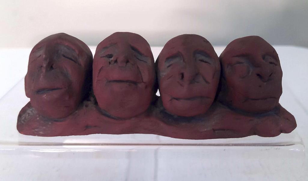 Ceramic Sculpture of Four Faces: Hand-built ceramic sculpture depicting four stylized human faces joined in a horizontal composition. Executed in reddish-brown clay with darkened accenting to the facial features, the work displays a 