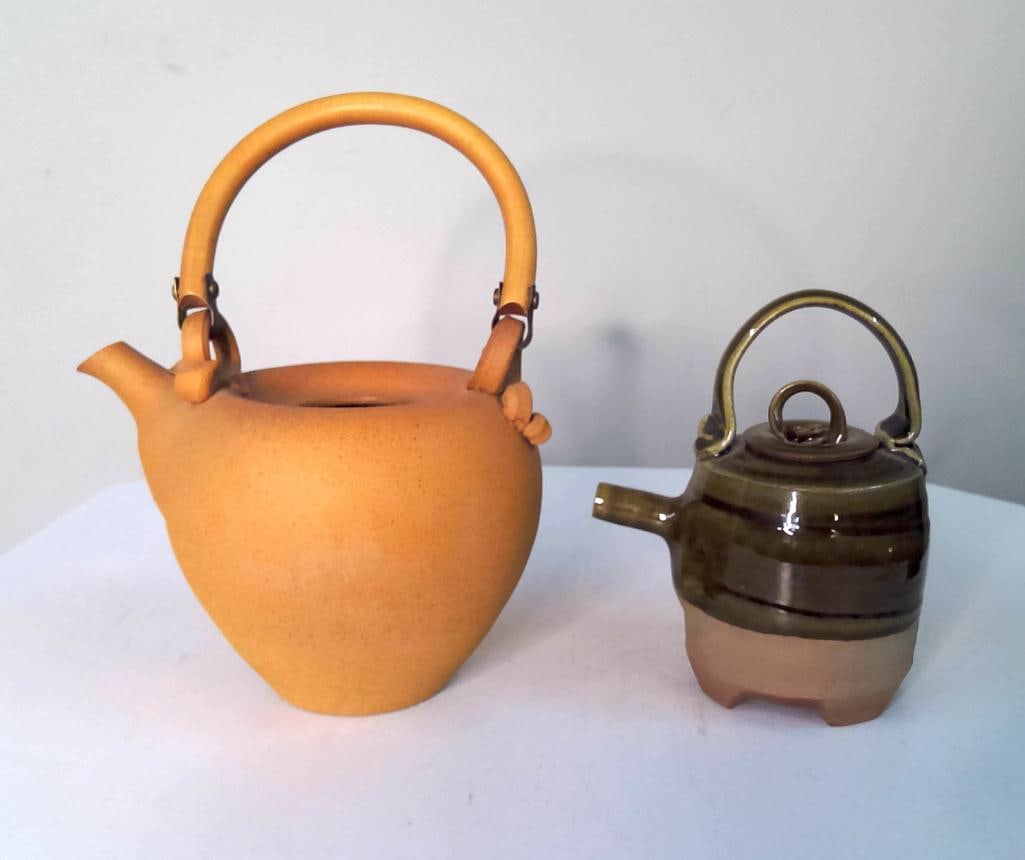 Sarah Frederick Pair of Studio Pottery Teapots: Group of two hand-thrown stoneware teapots by California studio potter Sarah Frederick. The larger example features an unglazed buff stoneware body with sculptural swing handle and integrated spout. T