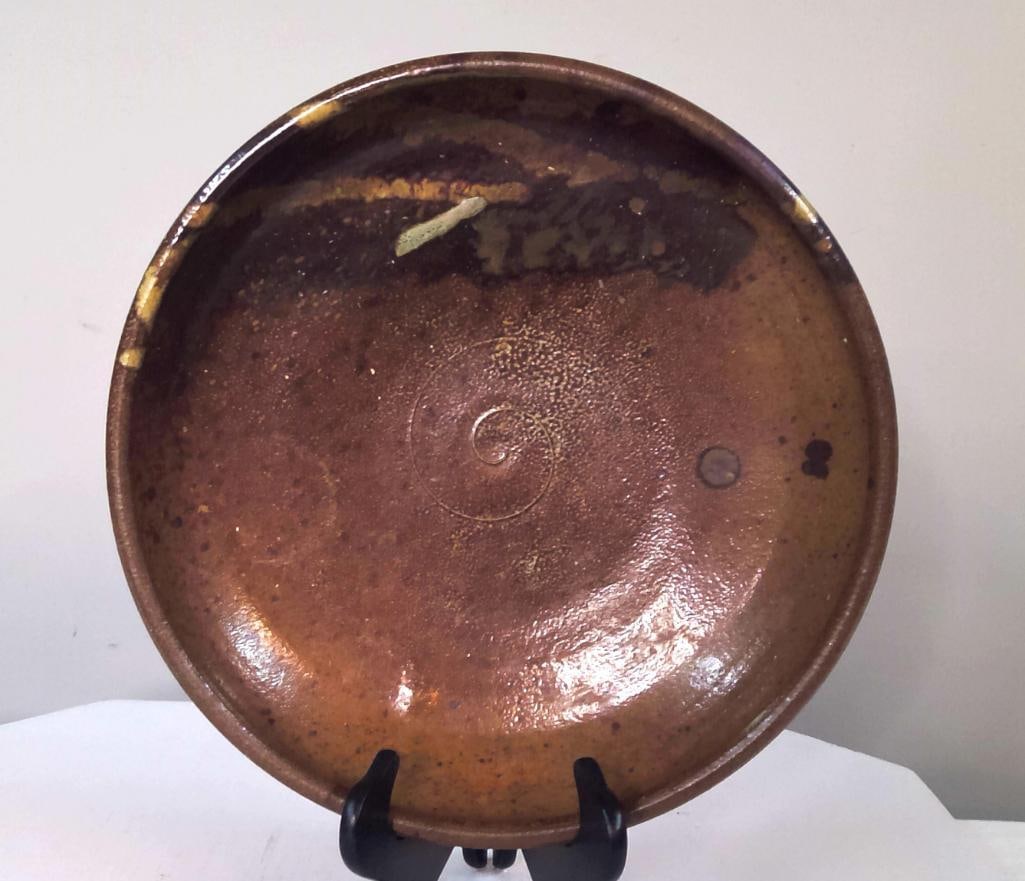 American Studio Pottery Brown Glazed Charger: Hand-thrown studio pottery charger featuring a rich iron-brown glaze with mottled surface decoration and an incised spiral motif to the center. The broad shallow form is finished with a rolled rim
