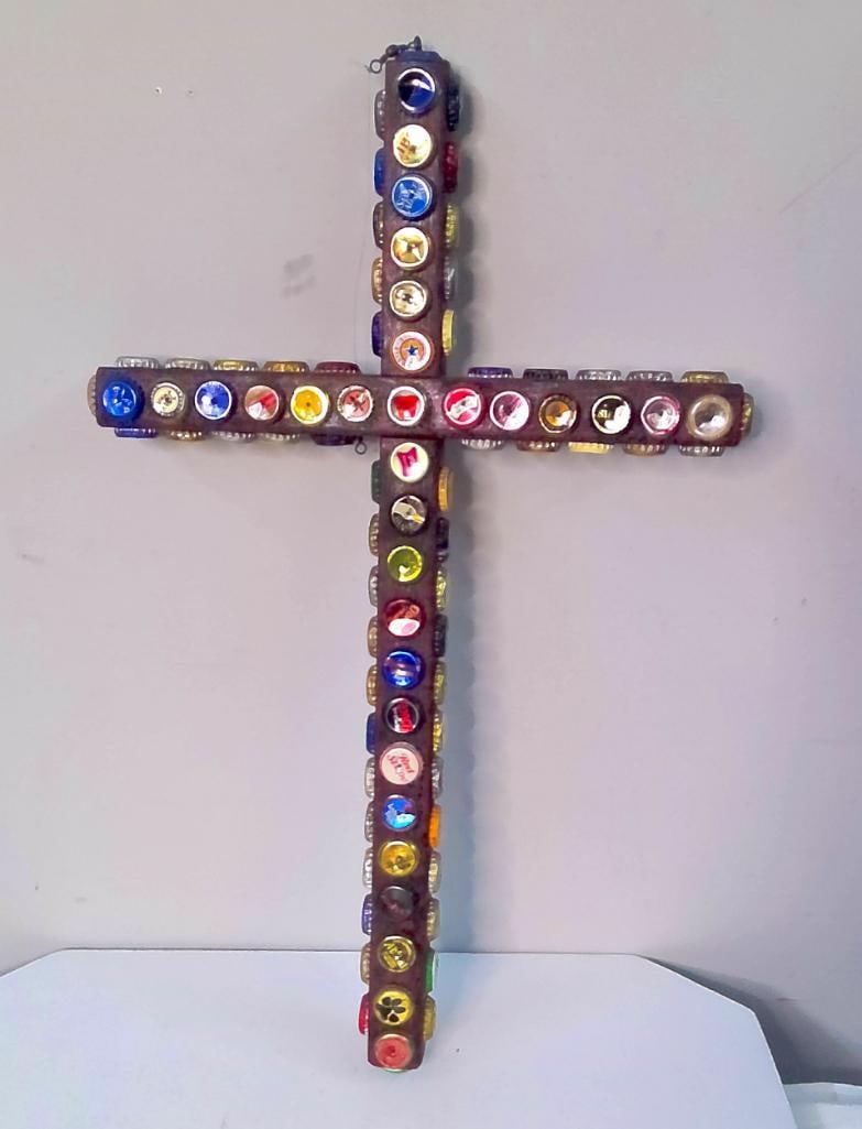 Unsigned Bottle-Cap Folk Art Cross: Unsigned American folk-art wall sculpture constructed from intersecting stained and painted wooden boards, densely ornamented on the front, sides, and ends with an assortment of vintage beer and soft-
