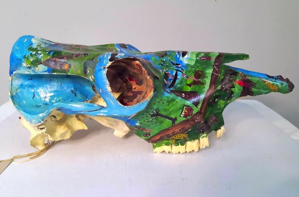 Jessie F. Cooper (Kentucky, 1932–2013): Indian Country, 1993, Paint on an animal skull, likely horse, depicting a continuous panoramic scene populated by stylized Indigenous figures, tipis, mounted riders, boats, wildlife, trees, waterways,