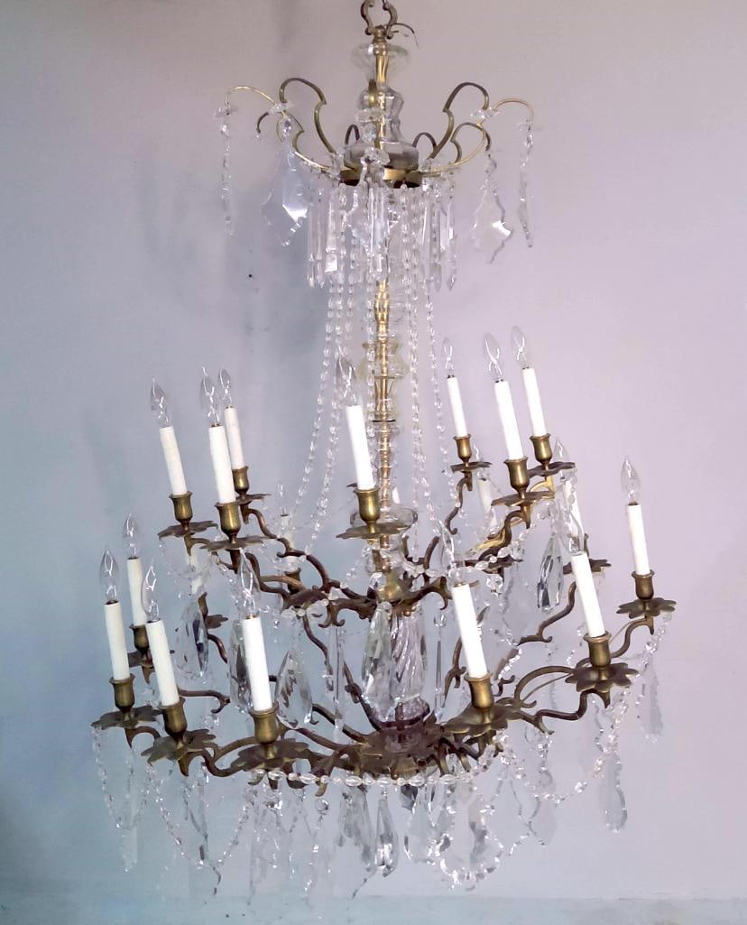 French Louis XV Style Crystal and Brass Eighteen-Light Chandelier: Circa Late 19th, early 20th C. Monumental Louis XV-style chandelier constructed of gilt brass and cut crystal elements. The fixture features eighteen candle-form sockets arranged on two graduated tier