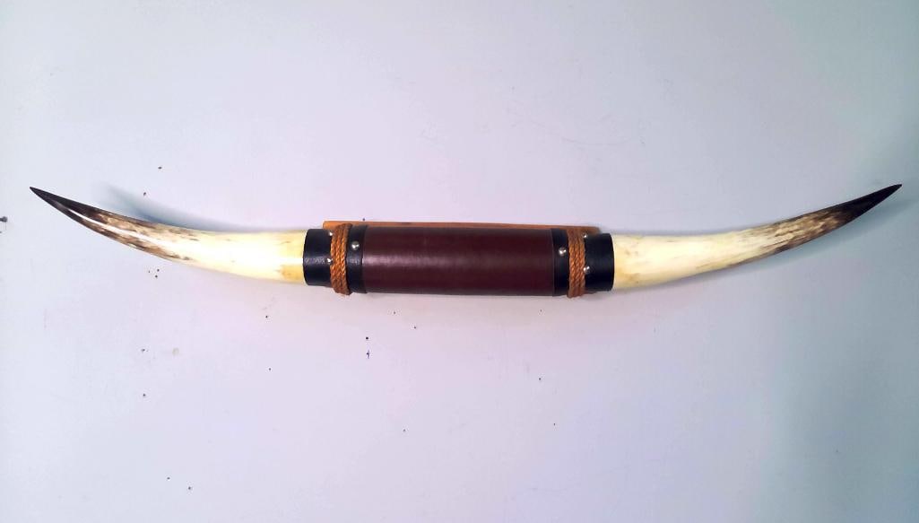 Mounted Steer Horns With Leather and Rope Accents: Pair of natural cattle horns mounted on a shaped wooden wall plaque. The horns display cream and brown mottling terminating in dark pointed tips. The center is wrapped in brown leather with black leat