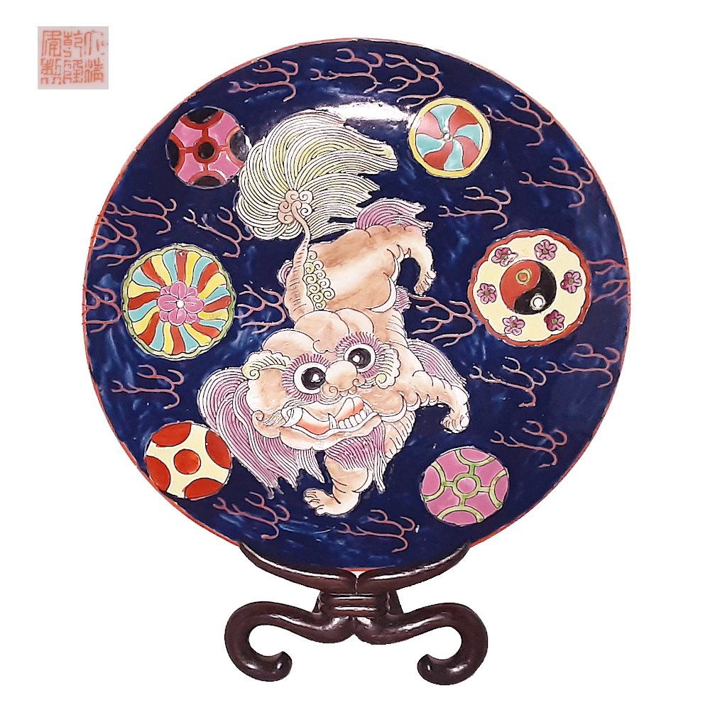 A DELIGHTFUL CHINESE PORCELAIN PLATE FOO LION QIANLONG: The whimsical enameled plate with a Foo lion on dark blue ground, with various balls. The plate bears a red Qianlong mark but it is from Republic era probably. It is 26 centimeters wide. On a rosewood