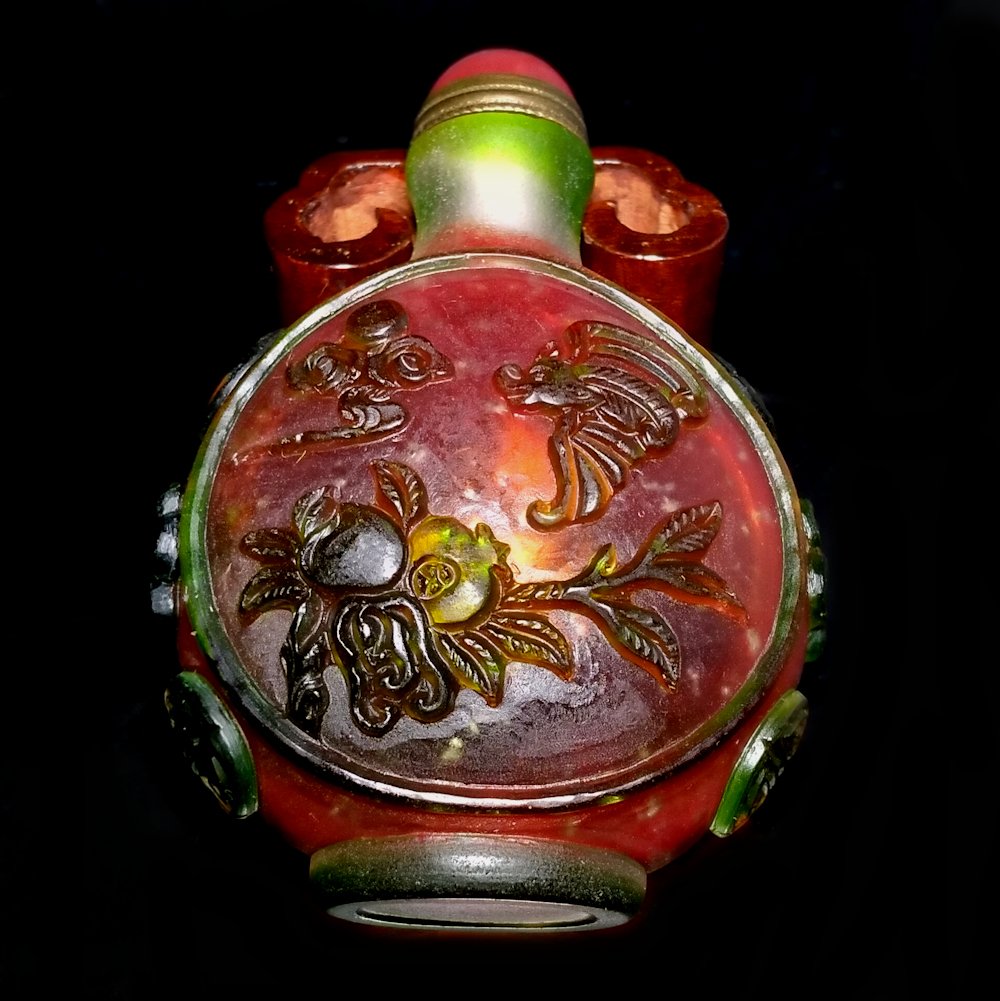 A FINE GLASS OVERLAY SNUFF BOTTLE 3 COLORS: THE FINE SNUFF BOTTLE IS SO FINELY AND ELABORATELY CARVED IN 3 LAYERS OF COLORS. BATS, POMEGRANATES AND A CITRON FRUIT. THERE ARE CARVED FLOWERS AND A SHOU SYMBOL AROUND THE SHOULDERS. THE MOUTH IS UN