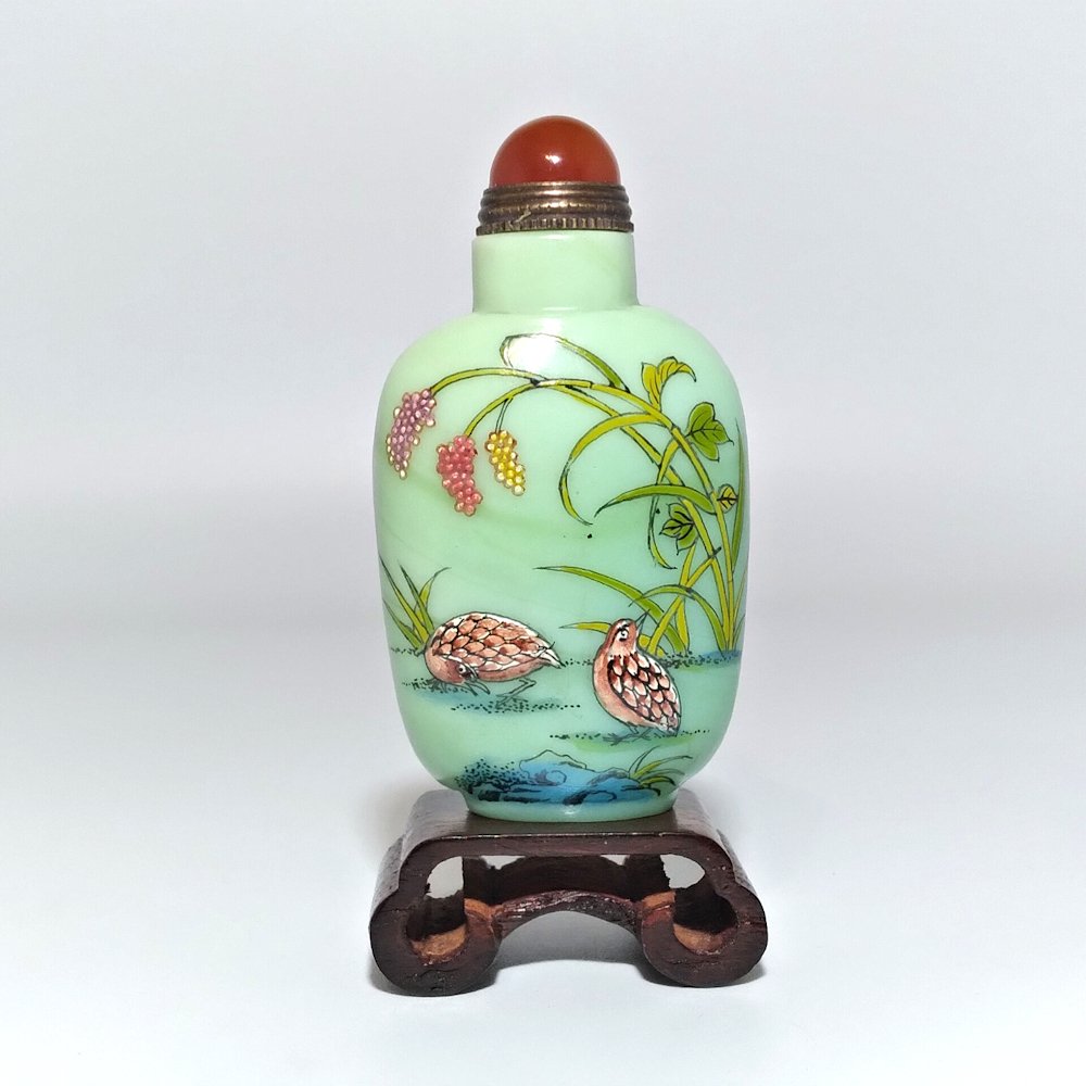 CHINESE ENAMEL GLASS SNUFF BOTTLE QUAILS: THE BEAUTIFULLY ENAMELED BOTTLE FEATURES QUAILS IN RELIEF, REEDS BAMBOO, PEONIES AND A BIRD. THE BOTTLE BEARS A CARNELIAN STOPPER. IT IS 3 INCHES TALL. PROVENANCE: PRIVATE FLORIDA COLLECTION.