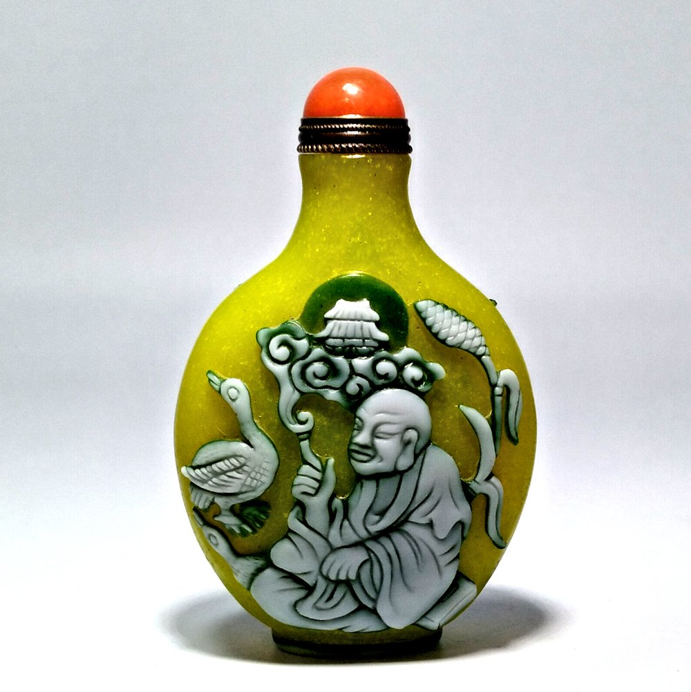 OUTSTANDING PEKING GLASS SNUFF BOTTLE LUOHAN: THE EXCELLENT AND RARE BOTTLE CARVED IN THREE LAYERS OF GLASS, WITH A YELLOW BACKGROUND. IT IS ARTIST SIGNED AND FEATURES LUOHANS. THE BOTTLE IS 3.2 INCHES TALL. PROVENANCE: PRIVATE FLORIDA COLLECTION