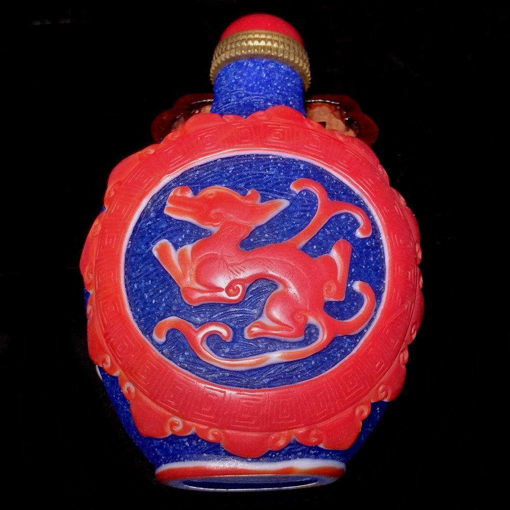 CHINESE OVERLAY GLASS SNUFF BOTTLE CHILUNG: A lovely glass snuff bottle featuring three layers of carved glass in red white and blue. The background is etched with a wave pattern. The bottle features two chi dragons. 3.2 inches tall.