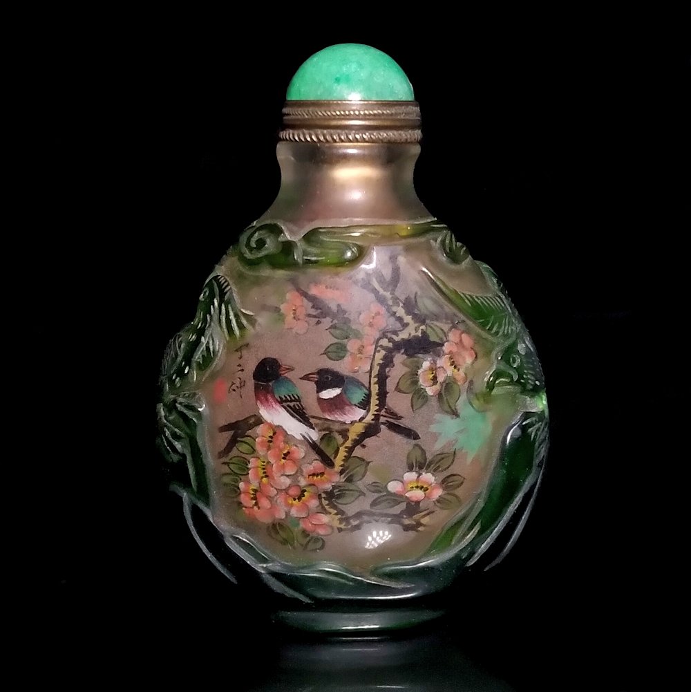 SIGNED CARVED PEKING GLASS INSIDE PAINTED SNUFF BOTTLE: THE BOTTLE IS SO BEAUTIFULLY CARVED ON THE SIDES WITH IMAGES OF PHOENIX, ROCKS AND BRANCHES. IT DEPICTS IMAGES WITH BIRDS AND IT IS SIGNED BY THE ARTIST. THE BOTTLE IS 3 INCHES TALL.
