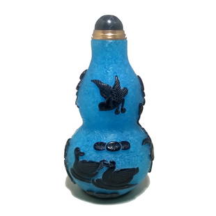 A FINELY CARVED CHINESE PEKING GLASS SNUFF BOTTLE DUCKS LOTUS: THE FINE SNUFF BOTTLE IS WELL CARVED IN BLACK OVER BUBBLE INFUSED BLUE GLASS. IT DEPICTS DUCKS, WATER AND LOTUS. IT IS 3.25 INCHES TALL. THE FOOT IS WELL DEFINED AND THE STOPPER BEARS AN ONYX