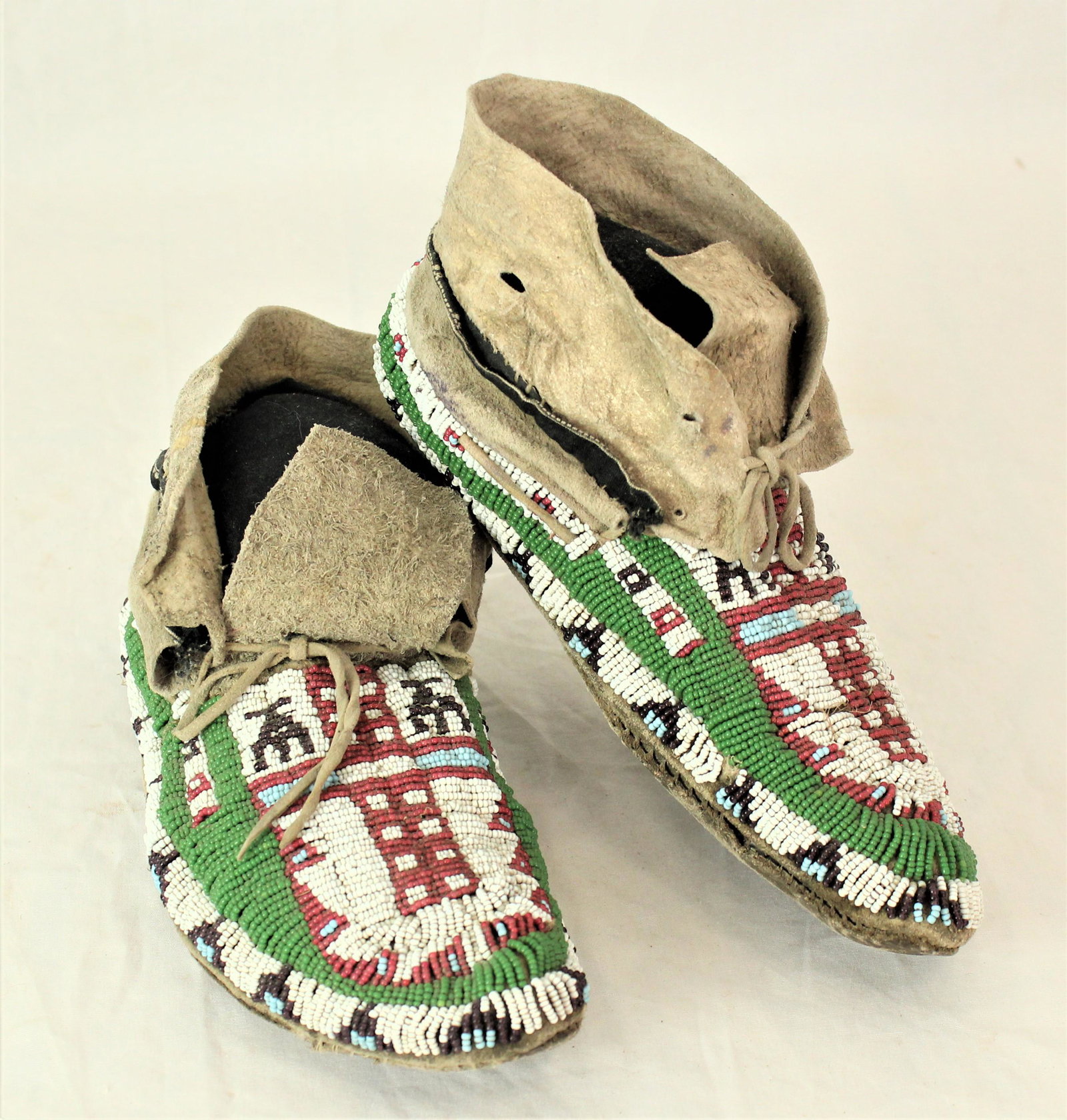 Arapahoe Moccasins: Exceptional early moccasins showing full coverage beadwork, having a terrific design of a large cross with thunderbirds on each side using translucent purple, white heart, and apple green beads. Measu