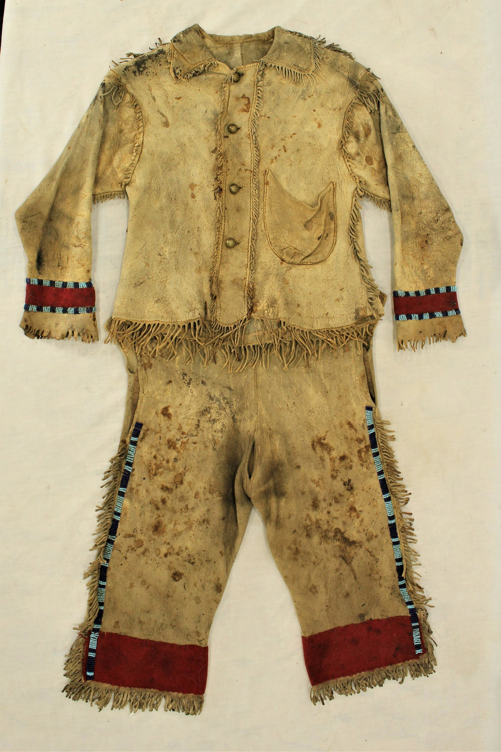 Crow Beaded Shirt & Pants: Phenomenal 1880's matching Crow Indian child's buckskin shirt and pants, with incredible condition and patina, wonderfully fringed throughout, with tradecloth cuffs and early beaded trim using translu