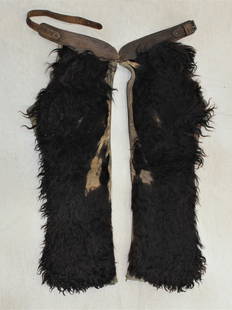 Angora Shotgun Chaps: An unmarked pair of black angora chaps with a basket stamped belt, showing cowboy character and wear.