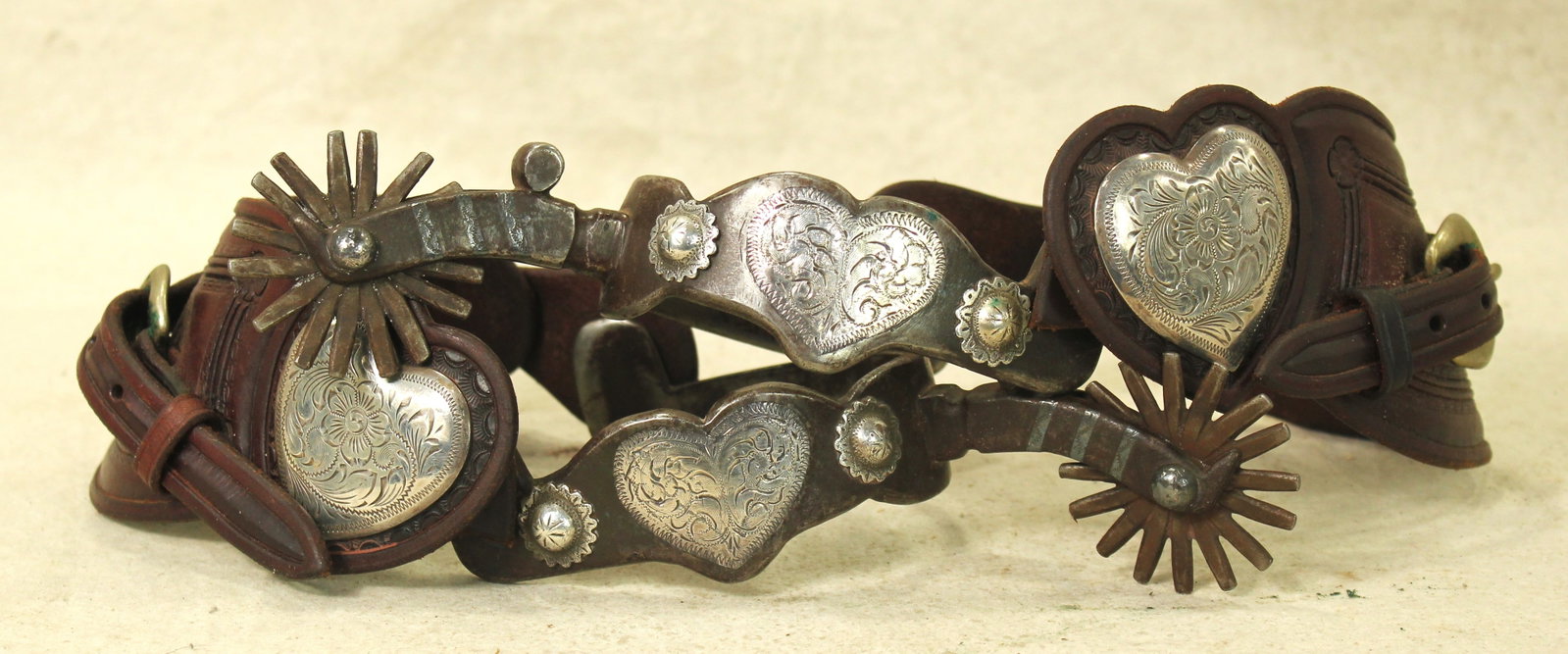 California Silver Spurs: A massive pair of single mounted spurs with scalloped heelbands centered around huge silver hearts, with detailed domes and multi-point rowels.