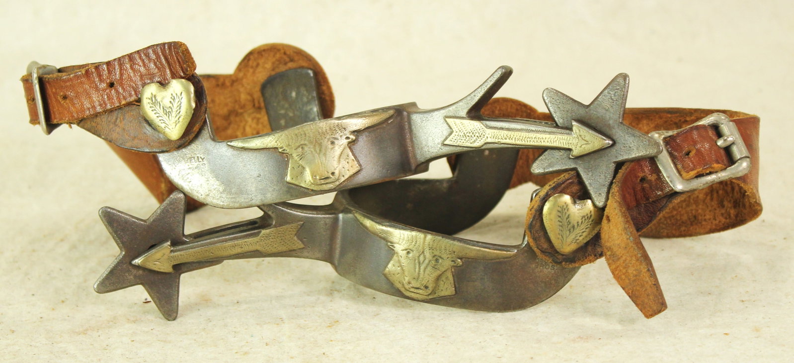 Kelly Bro's Bullhead Spurs: A large pair of classic cowboy spurs, single mounted with three dimensional steer heads, heart buttons, arrow shanks and large star rowels.