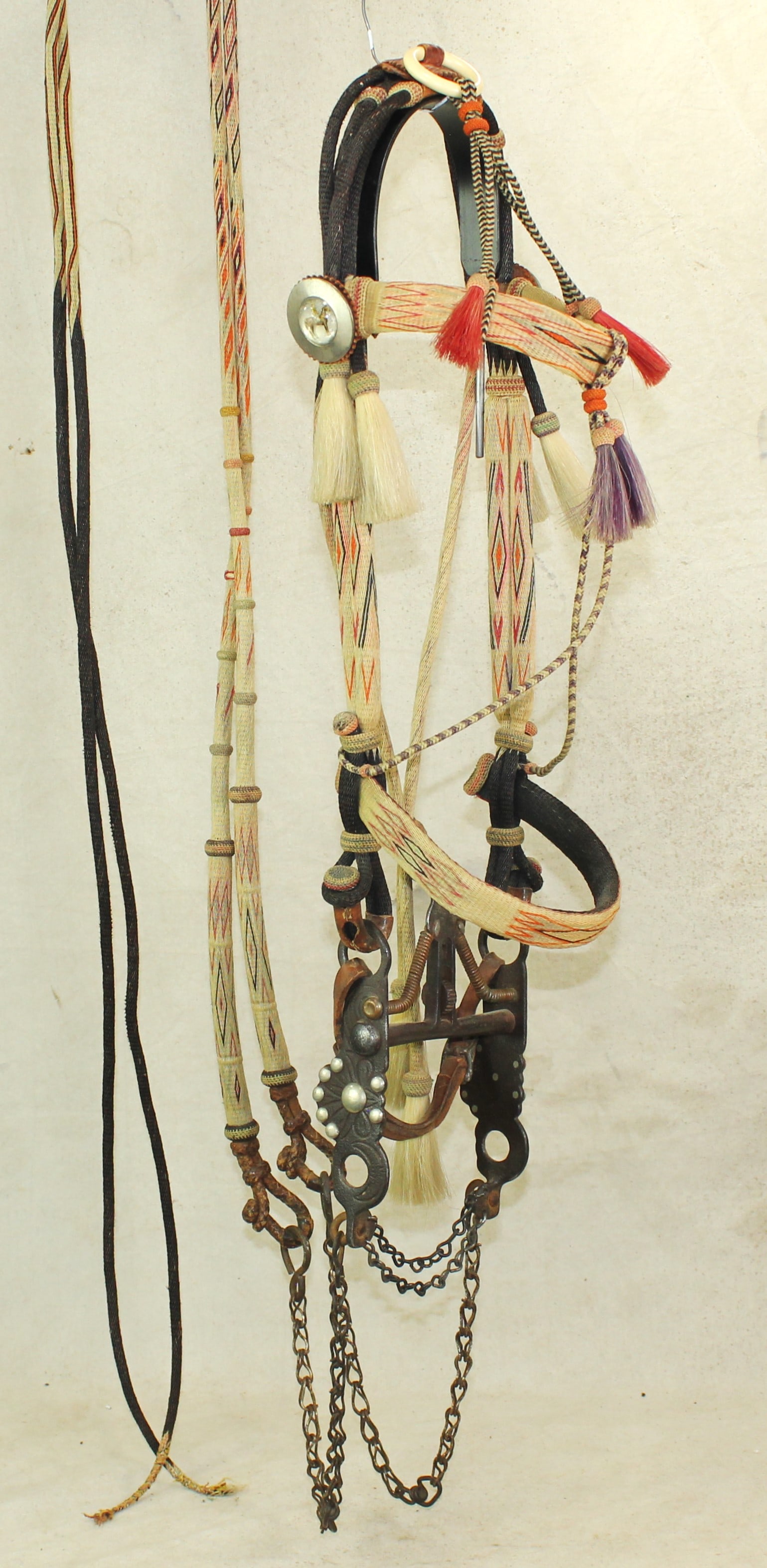 Deerlodge Prison Horsehair Bridle: A desirable 7 color Montana hitched horsehair bridle with brilliant colored tassles, glass rosettes, attractive double round cheeks, and colorful split reins, accented by a Buerman iron kissing bird s