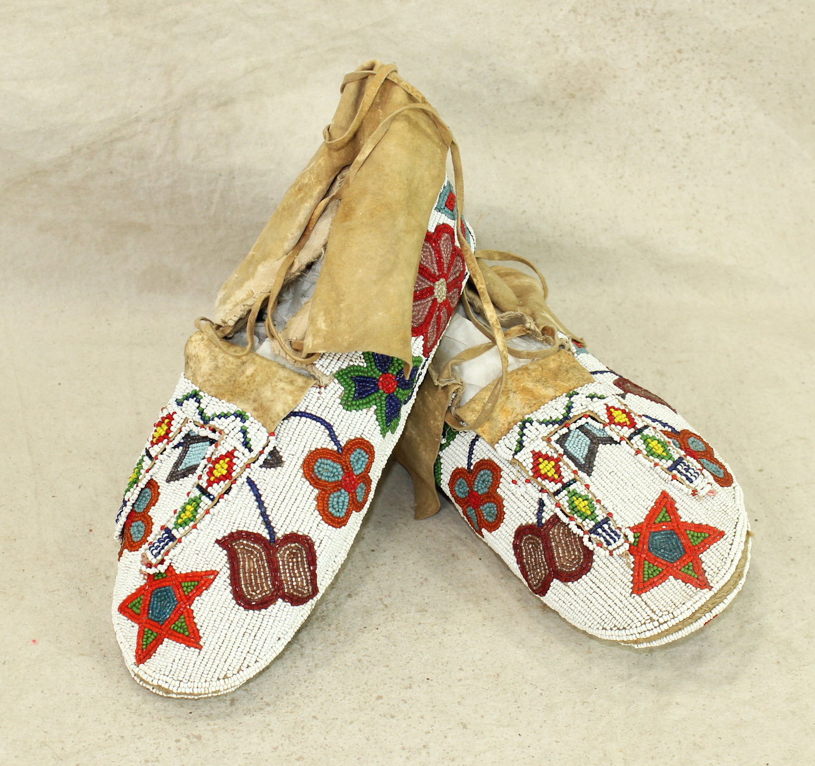 Incredible Ceremonial Moccasins: A brilliantly designed pair of Santee Sioux man's moccasins, circa 1900, with a great use of 13 different colors of beads in floral pattern, that extends to rare and desirable fully beaded ceremonial 