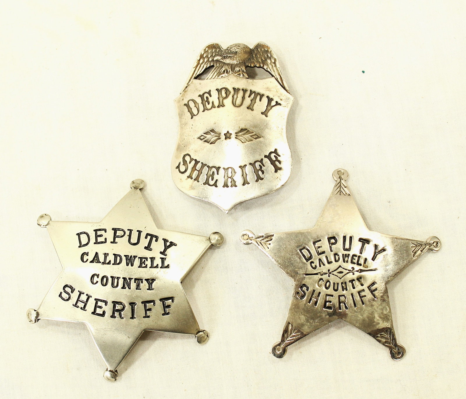 Lot of 3 Antique Badges: Three vintage deputy sheriff badges including Caldwell County examples and shield-form Deputy Sheriff badge. Mixed styles and manufacture dates.