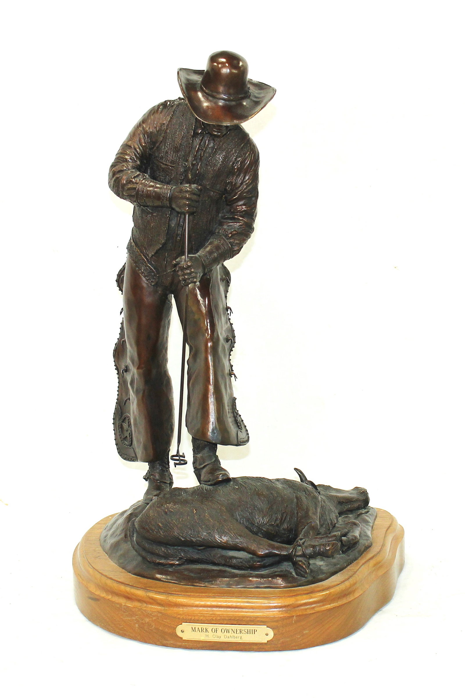 H. Clay Dahlberg Bronze: Bronze sculpture titled Mark of Ownership by noted Western artist H. Clay Dahlberg. Depicting a cowboy branding a steer, mounted on a custom wooden display base. Dimensions 22”x 10”x 10